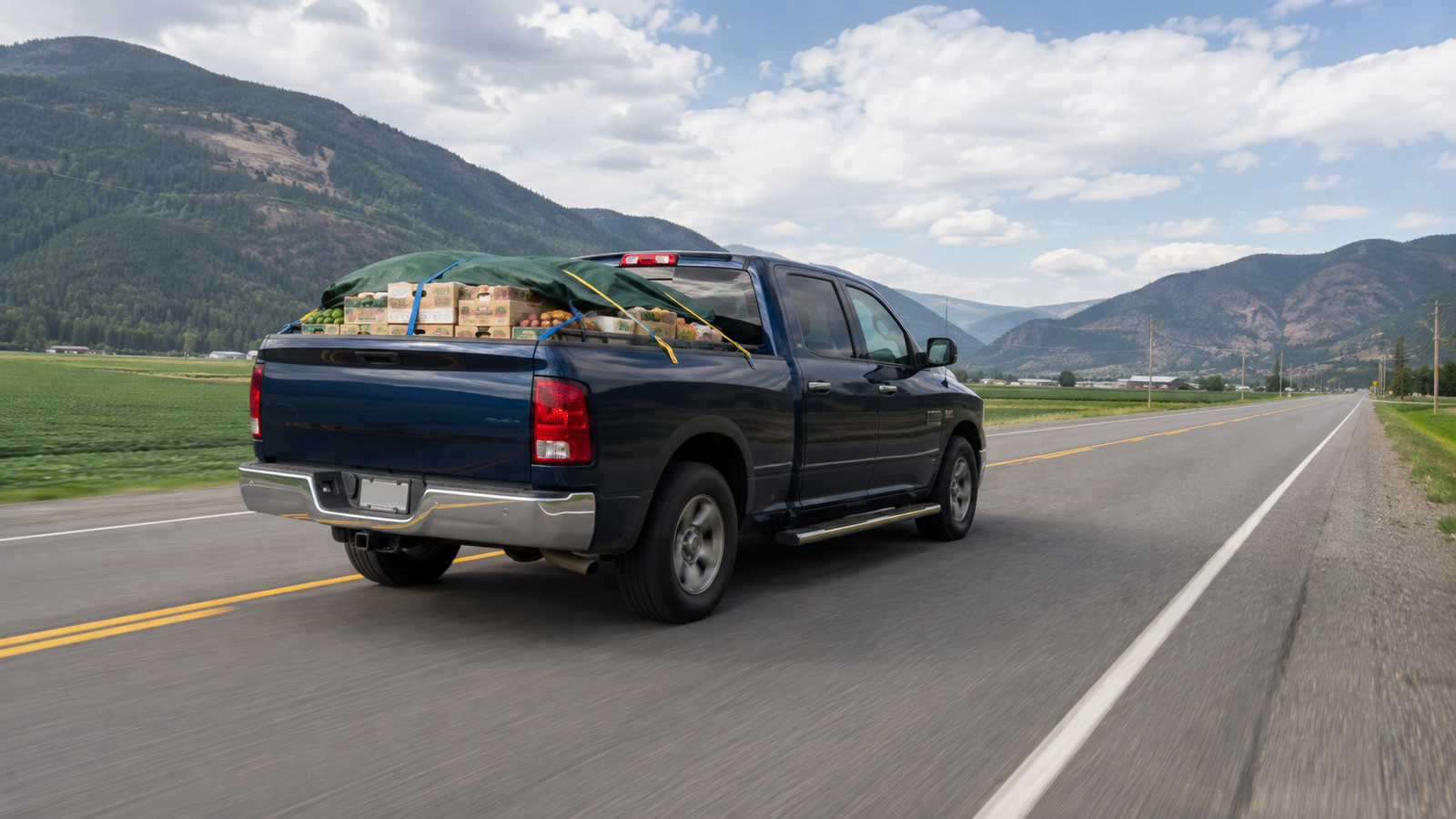 Canyon Runner Hotshot truck hauling strapped produce crates under green netting on a Creston Valley road, rear angle