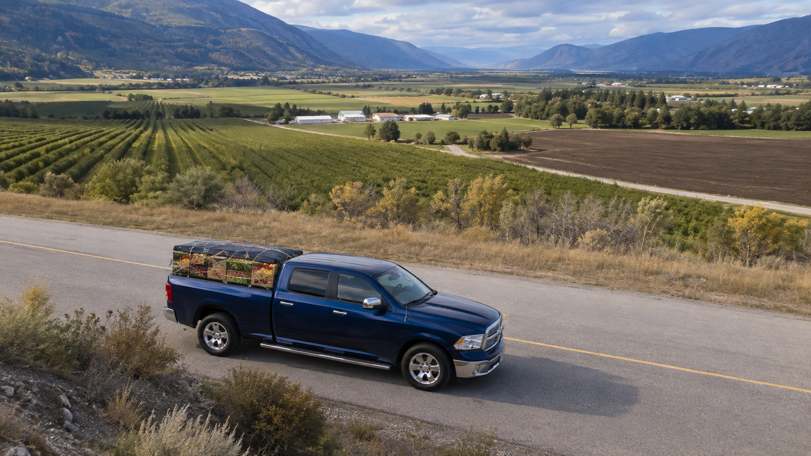 Canyon Runner Hotshot truck loaded with produce crates on a road above the Creston Valley orchards and farmland