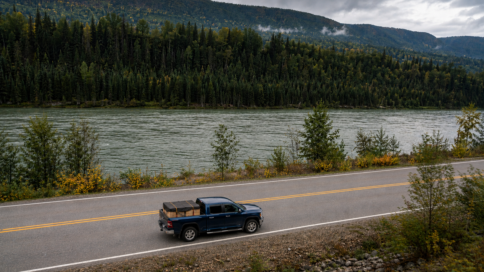 Aerial view of Canyon Runner Hotshot navy blue pickup truck loaded with cargo, driving along the Fraser River near Quesnel, BC in autumn