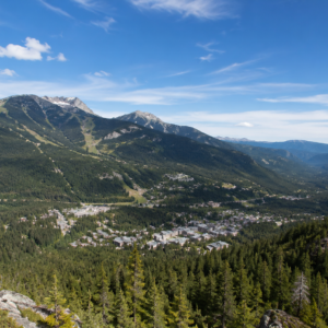 Elevated view over pine forest looking down on Whistler Village, BC, nestled in a mountain valley with a small lake and ski runs visible on the slopes beyond