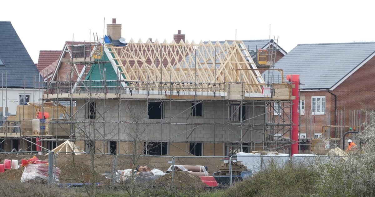 A wood-frame house under construction with roof trusses set, illustrating a residential framing project racing to close in before fall weather.