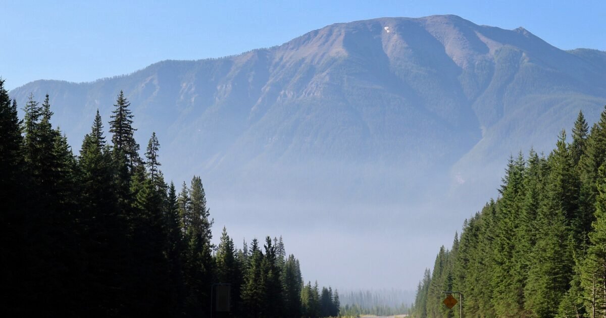A highway through forested mountains with wildfire smoke haze reducing visibility in the valley